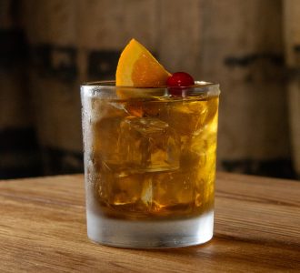 Image of Old Fashioned Cocktail in front of Bourbon Barrel
